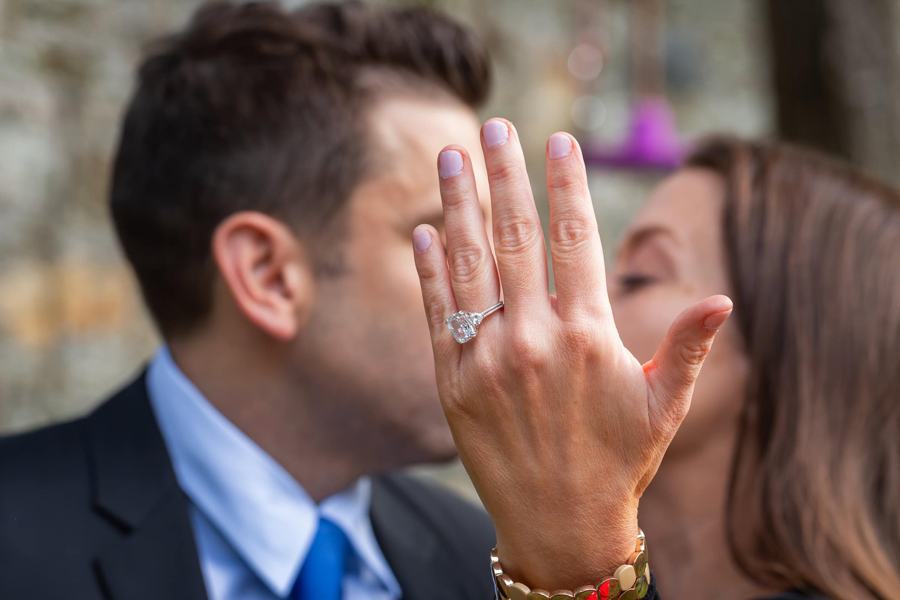 A couple kisses behind her hand, her engagement ring on show