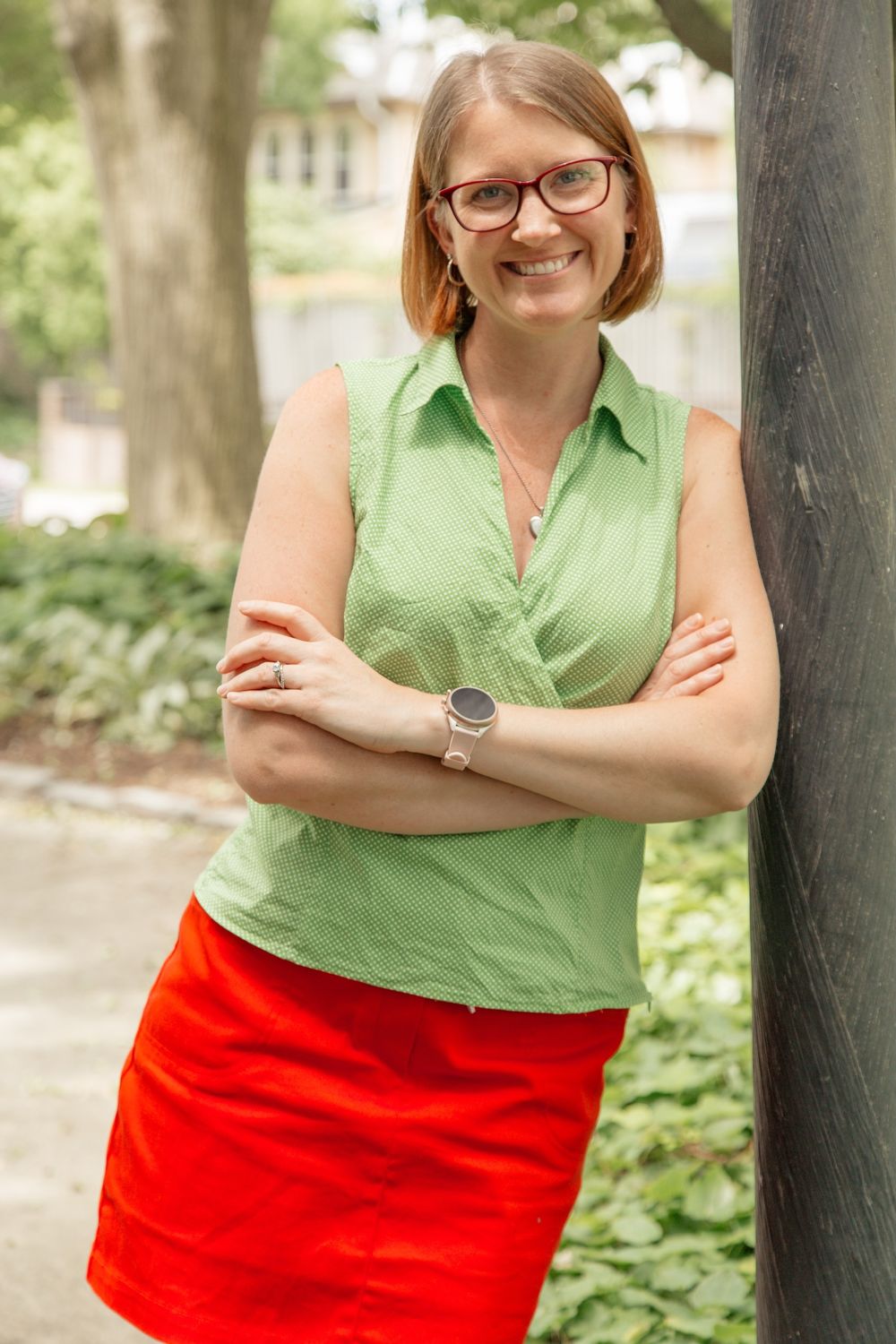 Sierra Clark, leaning against a tree in a green top and red skirt